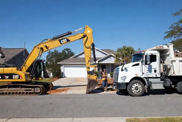 Post-storm cleanup completed in Orange Park Clay County Florida showing cleared driveway, restored roofline, and debris removal with excavator and dump truck finishing work